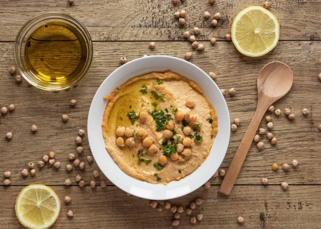 A bowl of creamy hummus topped with chickpeas, olive oil, and parsley - a nutrient-rich dish that supports adrenal function and mood regulation.
